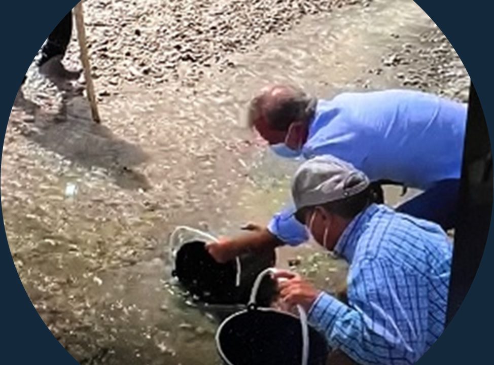 Dos funcionarios con mascarilla llenando cubos con agua y sedimento de río.