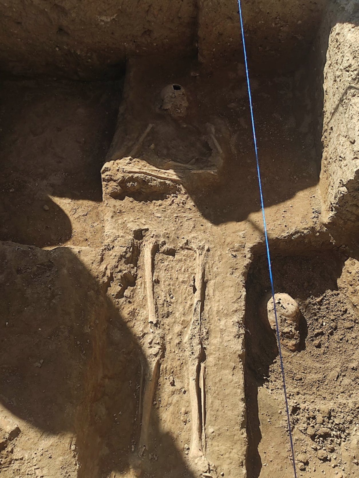 Restos humanos en una zanja de excavación, con una línea de reconocimiento cruzando el pozo.